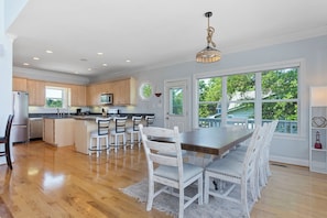 A spacious kitchen with wooden cabinets, a central island, and a dining area with white chairs and a large table. - Soundfront | Pool + Game Room + Private Pier (Emerald Isle)