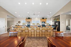 A spacious kitchen with a central island, bar stools, and a dining area with wooden tables. - 10BR Coastal Estate w/ Pool, Elevator, Game Rooms & Private Beach Access (Indian Beach)