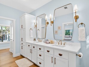 Une salle de bain avec un meuble-lavabo blanc, des accessoires dorés et un grand miroir.