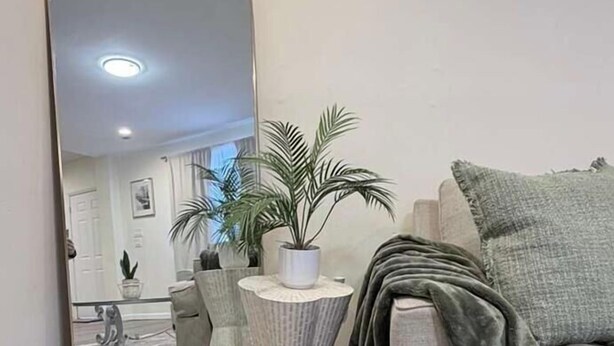 Ein Wohnzimmer mit einem großen Spiegel, einem grauen Sofa, einem kleinen runden Tisch mit einer Pflanze und einer grauen Decke.