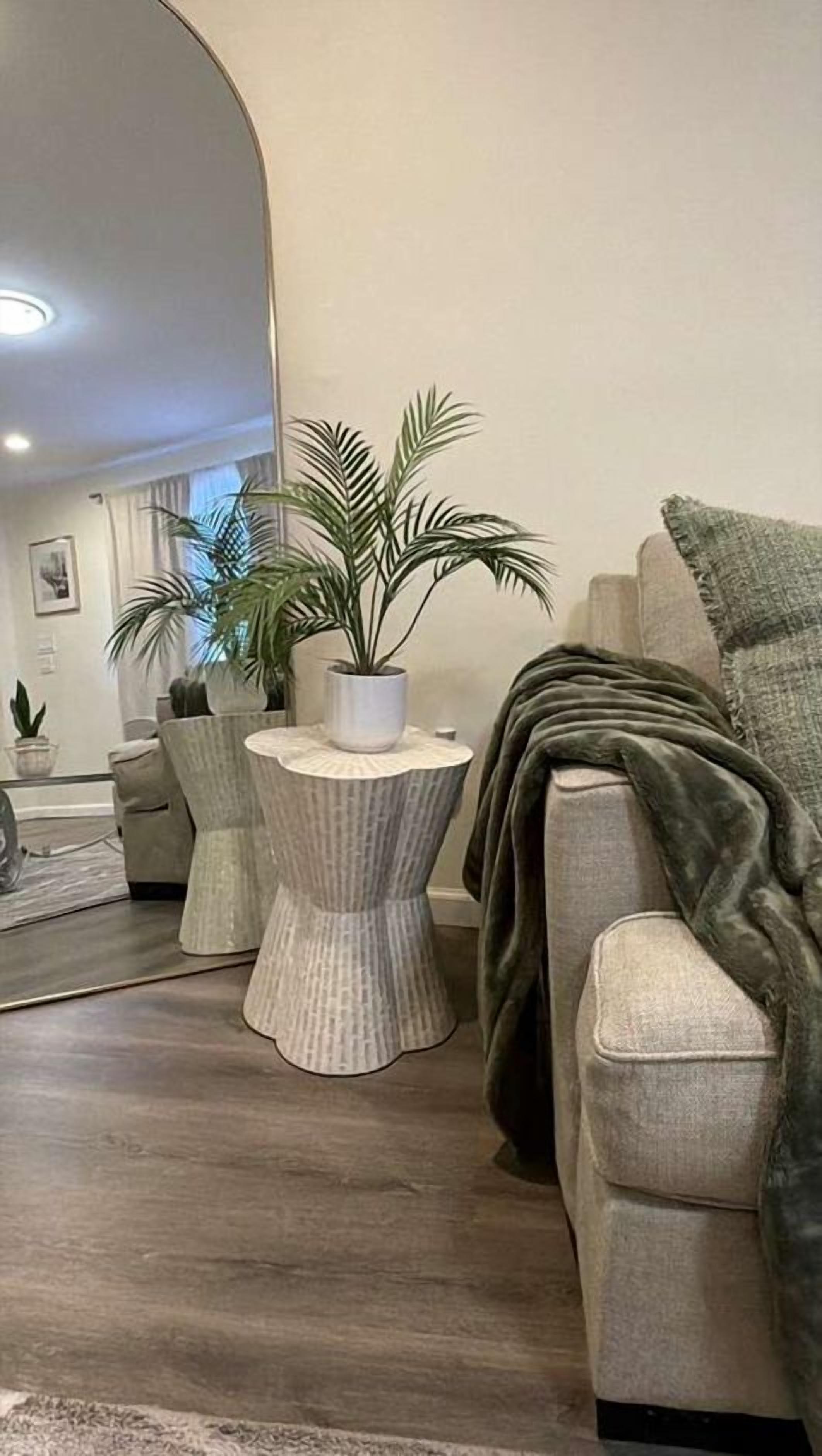 A modern living room with a grey sofa, a round side table with a potted plant, and a grey armchair with a throw blanket.