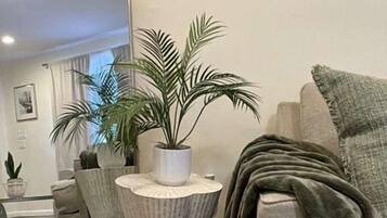 A modern living room with a grey sofa, a round side table with a potted plant, and a grey armchair with a throw blanket.