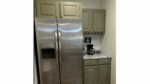Eine Küche mit einem Edelstahl-Kühlschrank, einer Kaffeemaschine und hellgrünen Schränken.