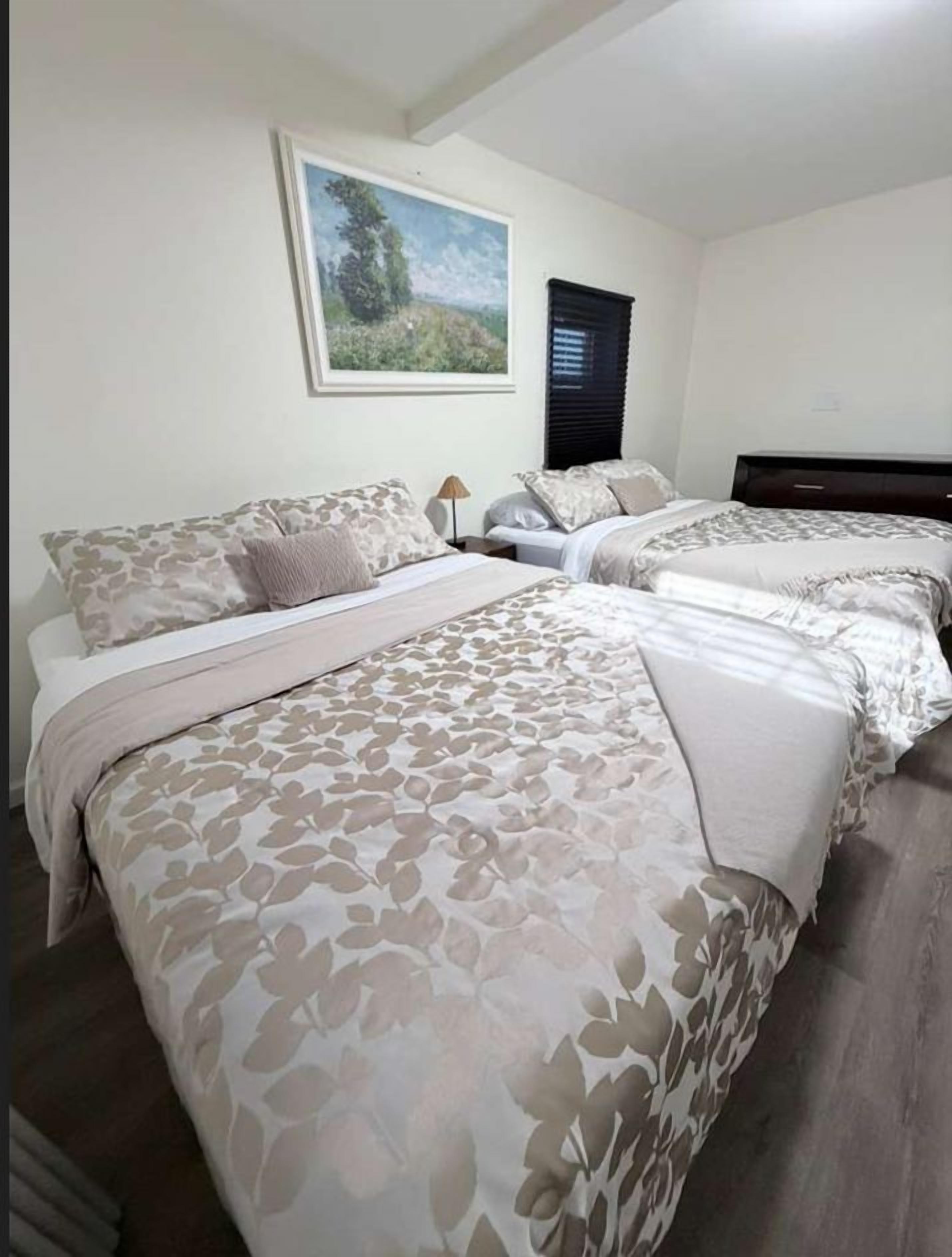 Una camera d'hotel con due letti, ognuno con biancheria da letto a motivi floreali, un comodino, una lampada e un quadro con un paesaggio appeso al muro.