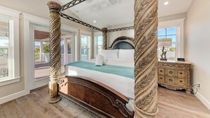 Un letto a baldacchino con testiera in marmo, un comodino in legno e vista verso il balcone esterno.