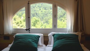 A room with two beds, each with green pillows, and a large arched window offering a view of a forested area. - Mountain, sports and wellness in Más El Prat (pet friendly) (La Pobla de Lillet)