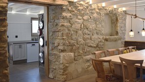 A kitchen with white cabinets, a dishwasher, and a stone wall. There is a dining area with wooden chairs and a table. - Mountain, sports and wellness in Más El Prat (pet friendly) (La Pobla de Lillet)