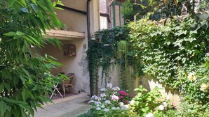Un jardín con un sendero de concreto, una silla de mimbre y diversas plantas, incluyendo rosas.