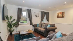 A living room with a sofa set, a coffee table, a TV mounted on the wall, and a window with curtains. - 6 Hallin Fell (Penrith)