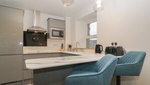 A modern kitchen with a central island, a microwave, a kettle, and a toaster. There are two blue bar stools at the island. - 6 Hallin Fell (Penrith)