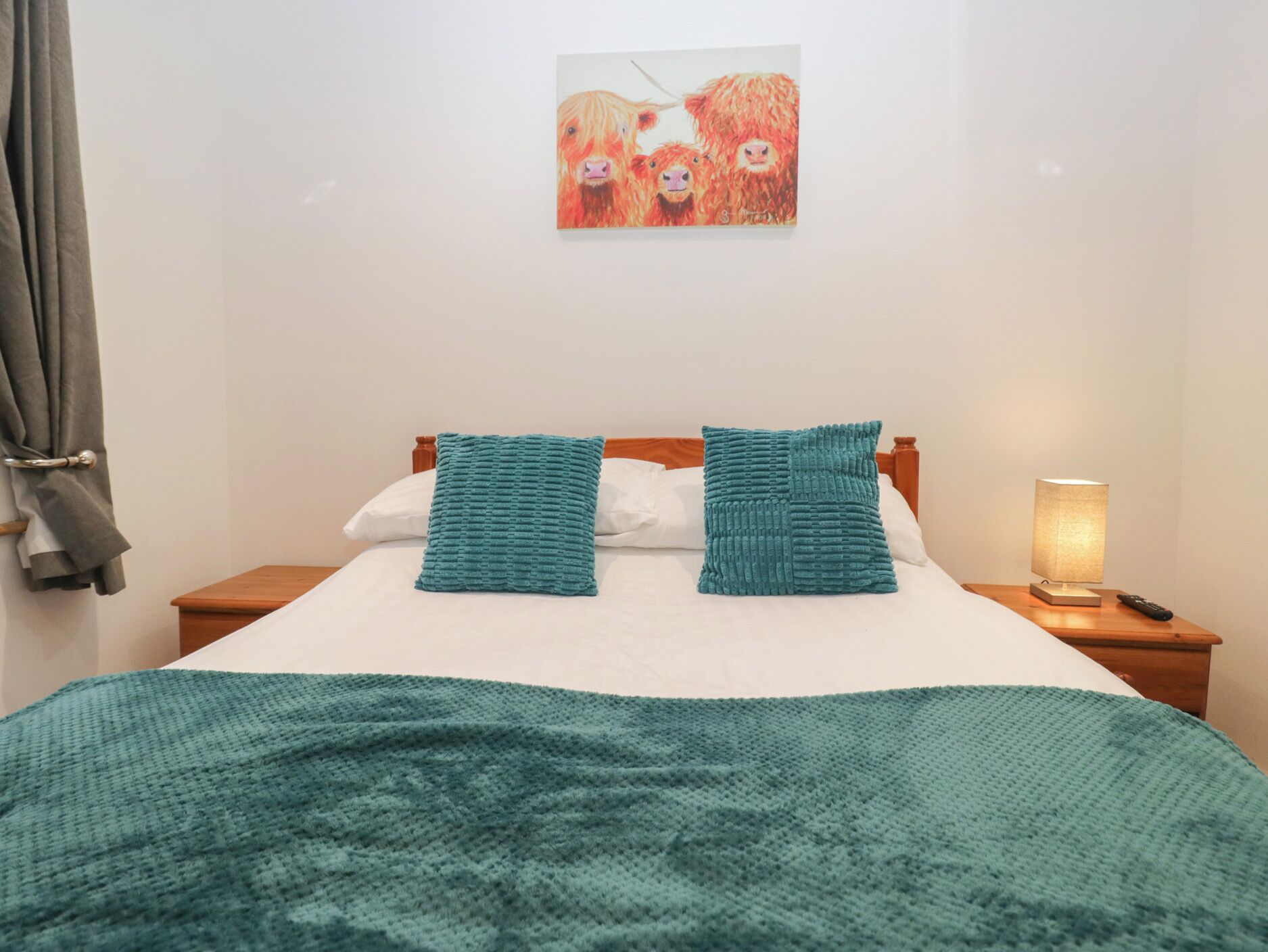 A neatly made bed with a teal blanket, two teal pillows, and a painting of animals on the wall.