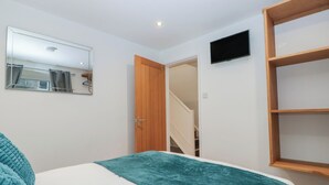 A bedroom with a bed, a mirror, a TV, and a wooden shelf. - 6 Hallin Fell (Penrith)