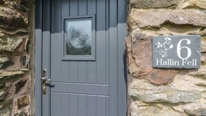 A grey door with a circular window and a stone wall with a house number sign. - 6 Hallin Fell (Penrith)