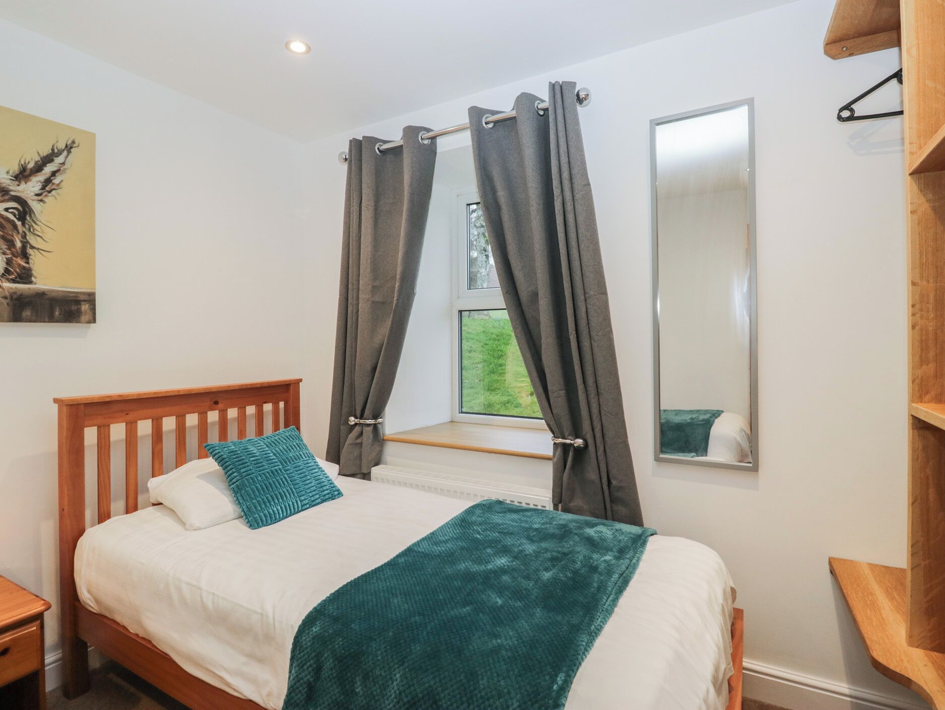 A bedroom with a wooden bed, white bedding, a teal throw blanket, and a window with curtains.