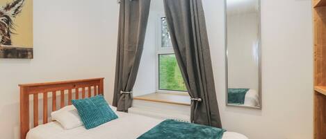 A bedroom with a wooden bed, white bedding, a teal throw blanket, and a window with curtains.
