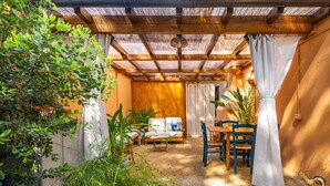 Ein überdachter Patio-Bereich mit Holzboden, einer Couch, Stühlen und einem Tisch.