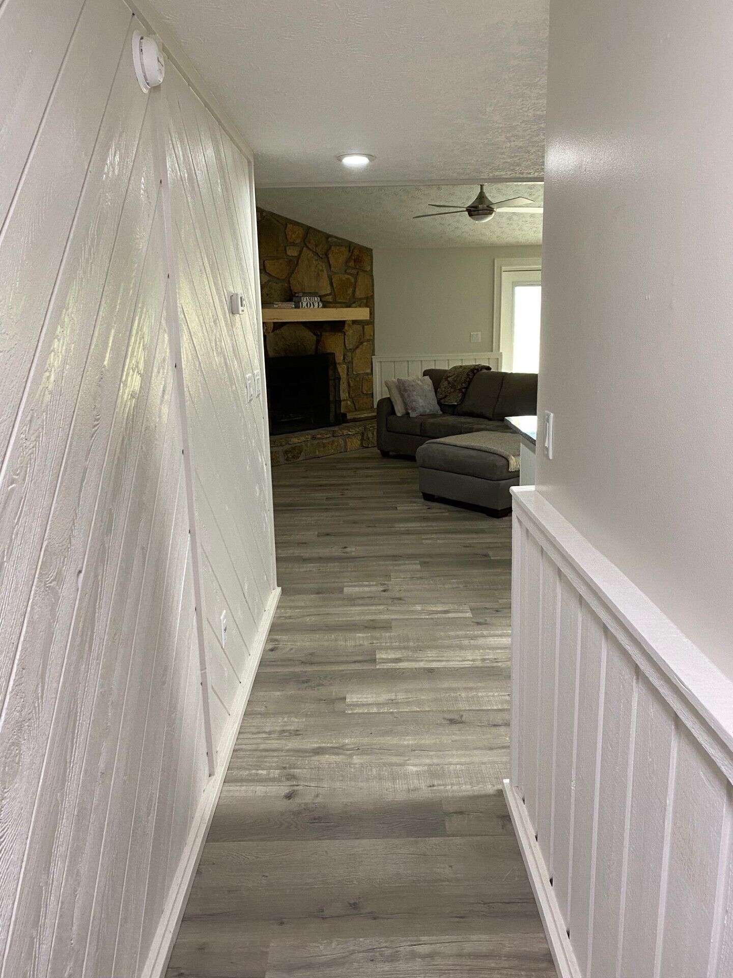 A hallway with a stone fireplace, a gray sofa, and a ceiling fan.