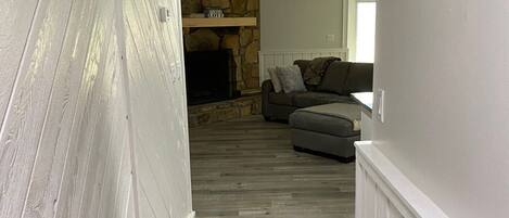 A hallway with a stone fireplace, a gray sofa, and a ceiling fan.