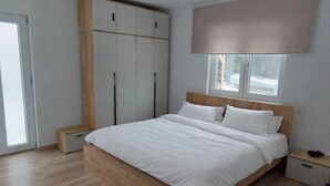 Un dormitorio con estructura de cama de madera, ropa de cama blanca, un armario con varias puertas y una ventana con vistas al exterior.