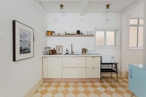 A kitchen with white cabinets, a checkered floor, a framed picture, and a window with blinds. - Chill Place in the City: Rua Augusta x Paulista x Frei Caneca (São Paulo)
