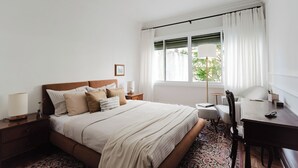 Ein ordentlich eingerichtetes Schlafzimmer mit Bett, Nachttischen, Schreibtisch und einem Fenster mit Vorhängen.