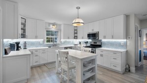 A modern kitchen with white cabinetry, a central island with a sink, and a pendant light. - Grace Cottage, St Michaels Walk to everything! (Saint Michaels)