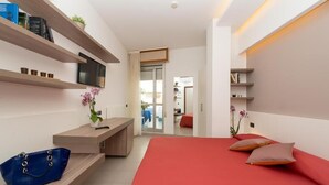 A modern hotel room with a red bed, a TV on a shelf, a desk with a chair, and a blue handbag on the floor. - Zenit Hotel (Giulianova)