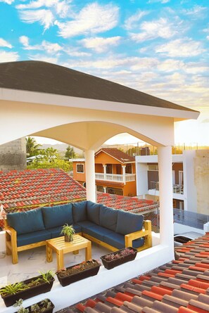 A covered outdoor seating area with a sofa, coffee table, and planters. - Agapimou Apartments H (Gaspar Hernandez)