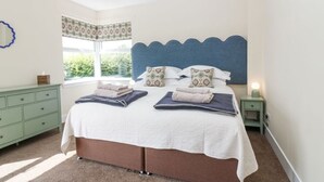 Un dormitorio con una cama grande, una ventana con cortinas estampadas, un aparador verde y una mesita de noche con una lámpara.