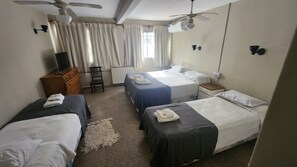 Habitación de hotel con dos camas, un aparador, una silla, ventilador de techo y ventana con cortinas.