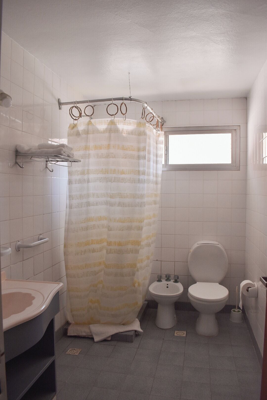 A bathroom with a shower curtain, a sink, a toilet, and a bidet.