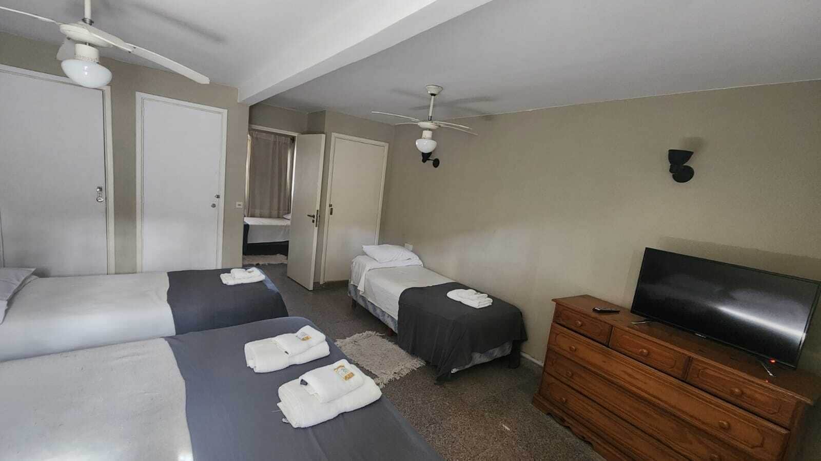 Habitación de hotel con dos camas, un televisor, un aparador de madera y un ventilador de techo.