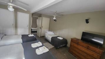Habitación de hotel con dos camas, un televisor, un aparador de madera y un ventilador de techo.