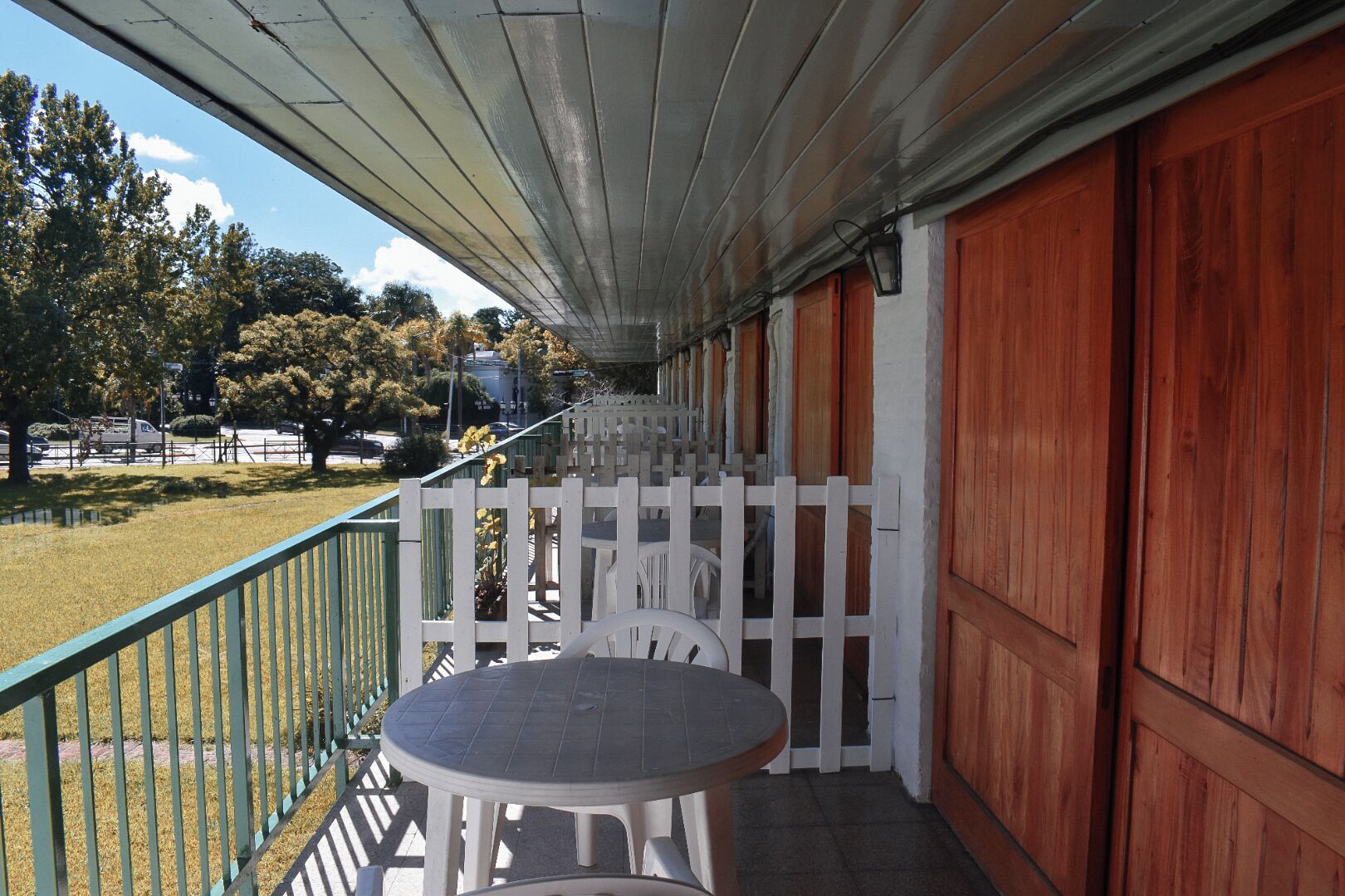 A covered outdoor area with a table and chairs, a white picket fence, and a view of the surrounding landscape.