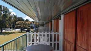 A covered outdoor area with a table and chairs, a white picket fence, and a view of the surrounding landscape.