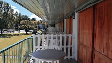 A covered outdoor area with a table and chairs, a white picket fence, and a view of the surrounding landscape.