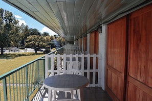 A covered outdoor area with a table and chairs, a white picket fence, and a view of the surrounding landscape.