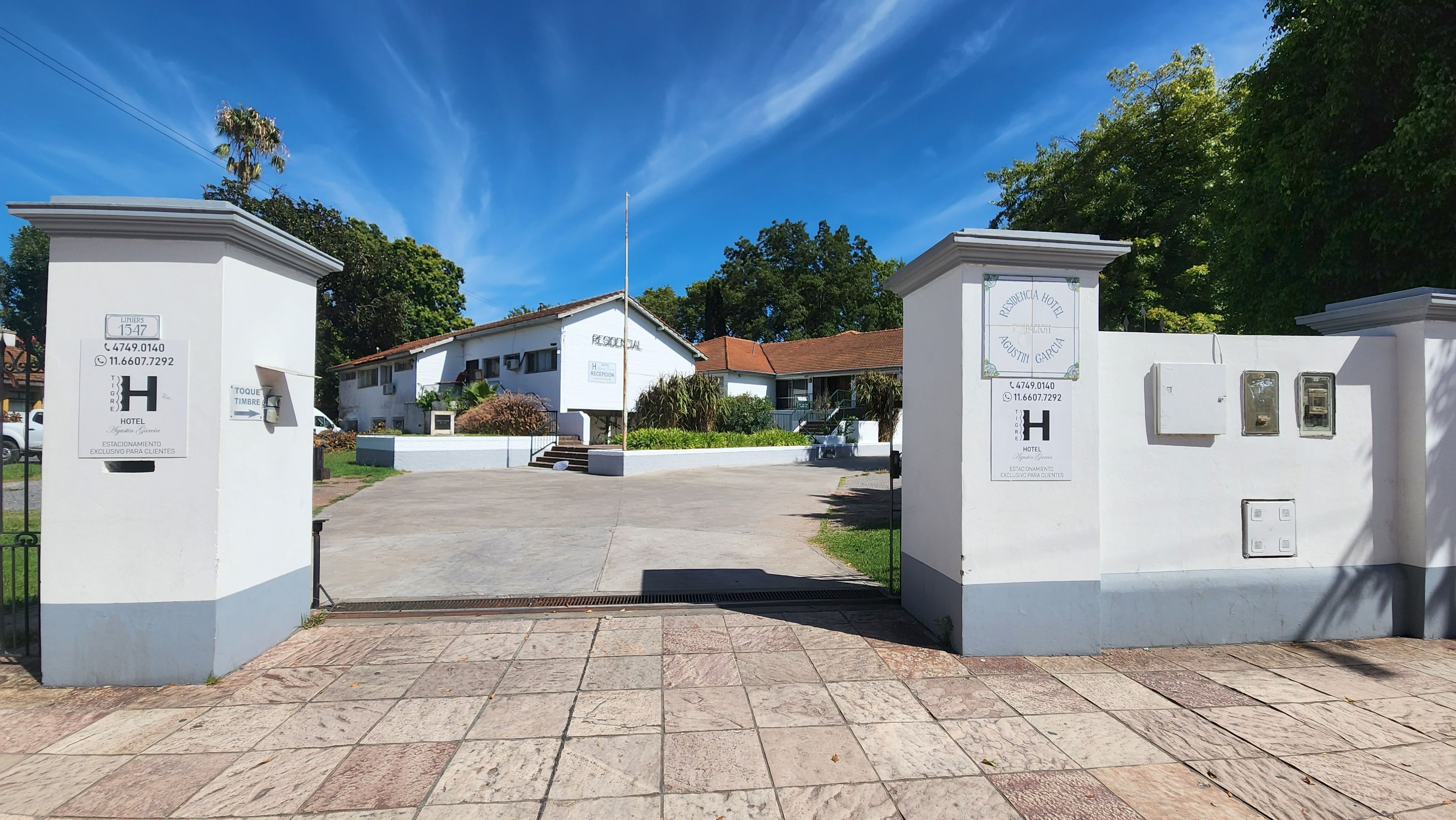 A hotel entrance with a gated driveway, a reception desk, and a building with a red roof.