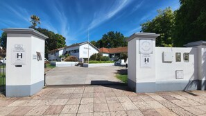 A hotel entrance with a gated driveway, a reception desk, and a building with a red roof. - Hotel Agustin Garcia (Tigre)