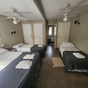Habitación de hotel con dos camas, un ventilador de techo y vistas al pasillo.