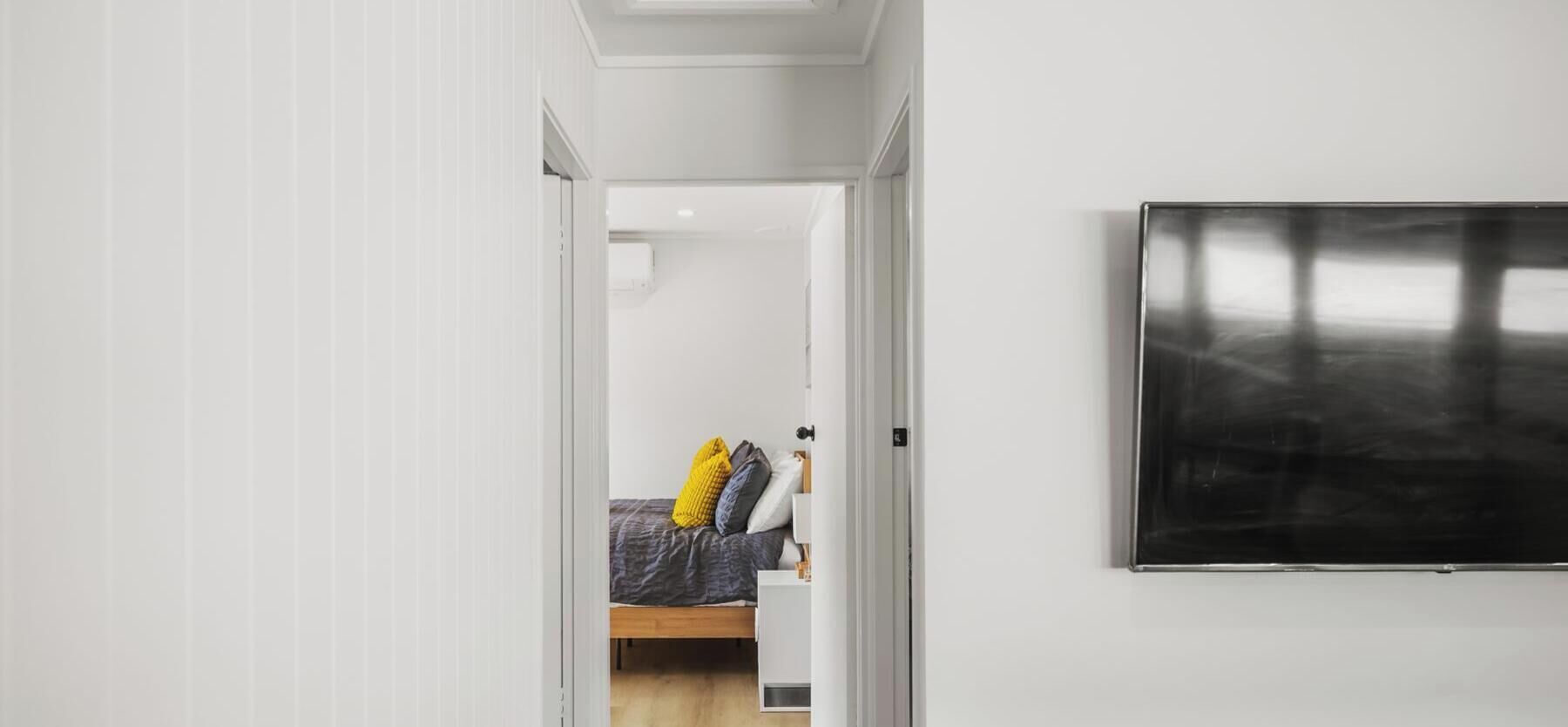 A hallway with a bed, a TV mounted on the wall, and a door leading to another room.