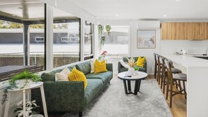 Eine moderne Küche mit Barbereich, einem grünen Sofa mit gelben Kissen und einem runden Tisch mit Stühlen.