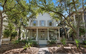 A two-story house with a covered porch, a front door, and a small garden area with mulch and plants. - Pelican & Palm - WaterColor Home & Golf Cart! (Santa Rosa Beach)