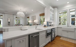A modern kitchen with white cabinetry, a stainless steel dishwasher, an oven, and a large island with a sink. - Pelican & Palm - WaterColor Home & Golf Cart! (Santa Rosa Beach)