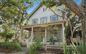 A two-story house with a covered porch, a staircase leading to the entrance, and a small garden area with plants and a pathway. - Pelican & Palm - WaterColor Home & Golf Cart! (Santa Rosa Beach)