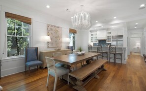 A modern kitchen with white cabinets, a stainless steel refrigerator, and a dining area with a wooden table and chairs. - Pelican & Palm - WaterColor Home & Golf Cart! (Santa Rosa Beach)