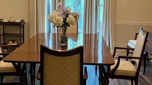 A dining room with a large wooden table, six chairs, a vase of flowers, and a view of greenery outside. - Spacious 4-bedroom house in charming Lawrenceville with AC (Lawrenceville)