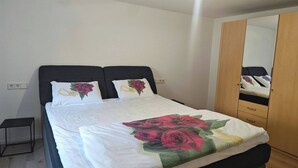 A neatly made bed with floral bedding, a bedside table, and a wardrobe with a mirror. - Charming Family Apartment in Wutöschingen With Garden View (Wutoeschingen)