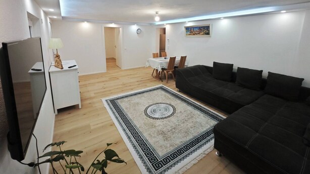 A modern living room with a black sofa, a white coffee table, and a patterned rug. - Charming Family Apartment in Wutöschingen With Garden View (Wutoeschingen)