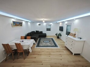 A compact living space with a dining area, a sofa, a TV, and a small cabinet. - Charming Family Apartment in Wutöschingen With Garden View (Wutoeschingen)